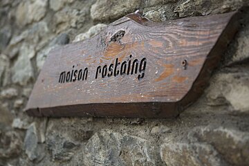 A wooden sign on a stone wall says maison postaing