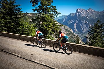 Two cyclists are riding down a road with mountains in the background