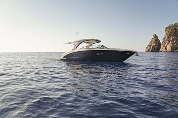 A dark Regal yacht floats on calm blue water, with rocky cliffs in the background under a clear sky.