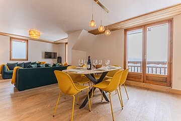 Modern open-plan living space with a dining table surrounded by yellow chairs, next to a living area with a dark green sofa.