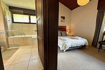 A cozy bedroom with a bed and an adjacent bathroom with a tub, seen through an open wooden door.