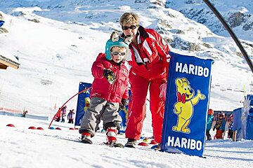 A woman is teaching a little boy how to ski in the snow
