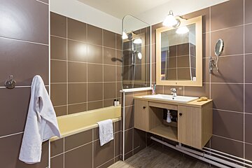 A bathroom with brown tiles and a sink and mirror