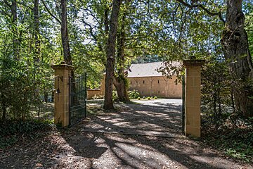A gated driveway leads to a building surrounded by trees