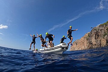A group of people jumping out of a boat that says ' scuba ' on the side