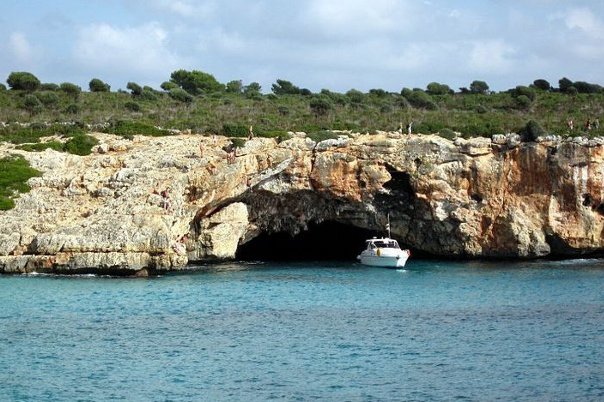 a boat in a sea cove with climbers on the rocks above