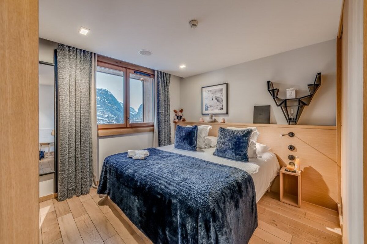 A bedroom with a bed and a window with mountains in the background
