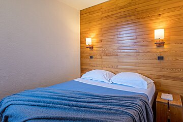 A bedroom with wood paneling and a bed with a blue blanket