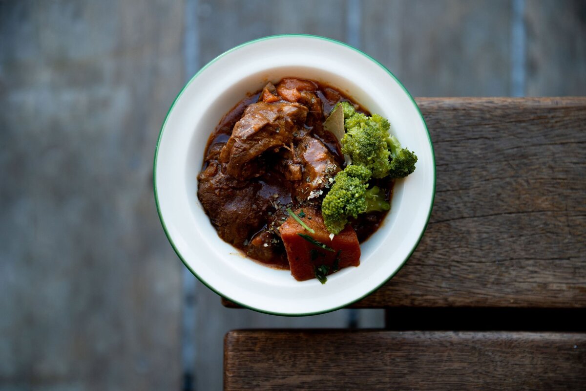 A bowl of stew with broccoli and carrots on a wooden table