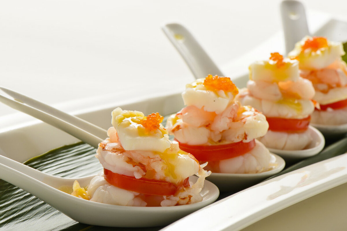 White spoons filled with shrimp and tomatoes on a plate