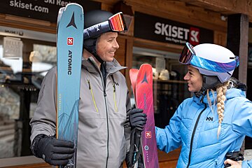 A man and a woman holding skis in front of a ski set store