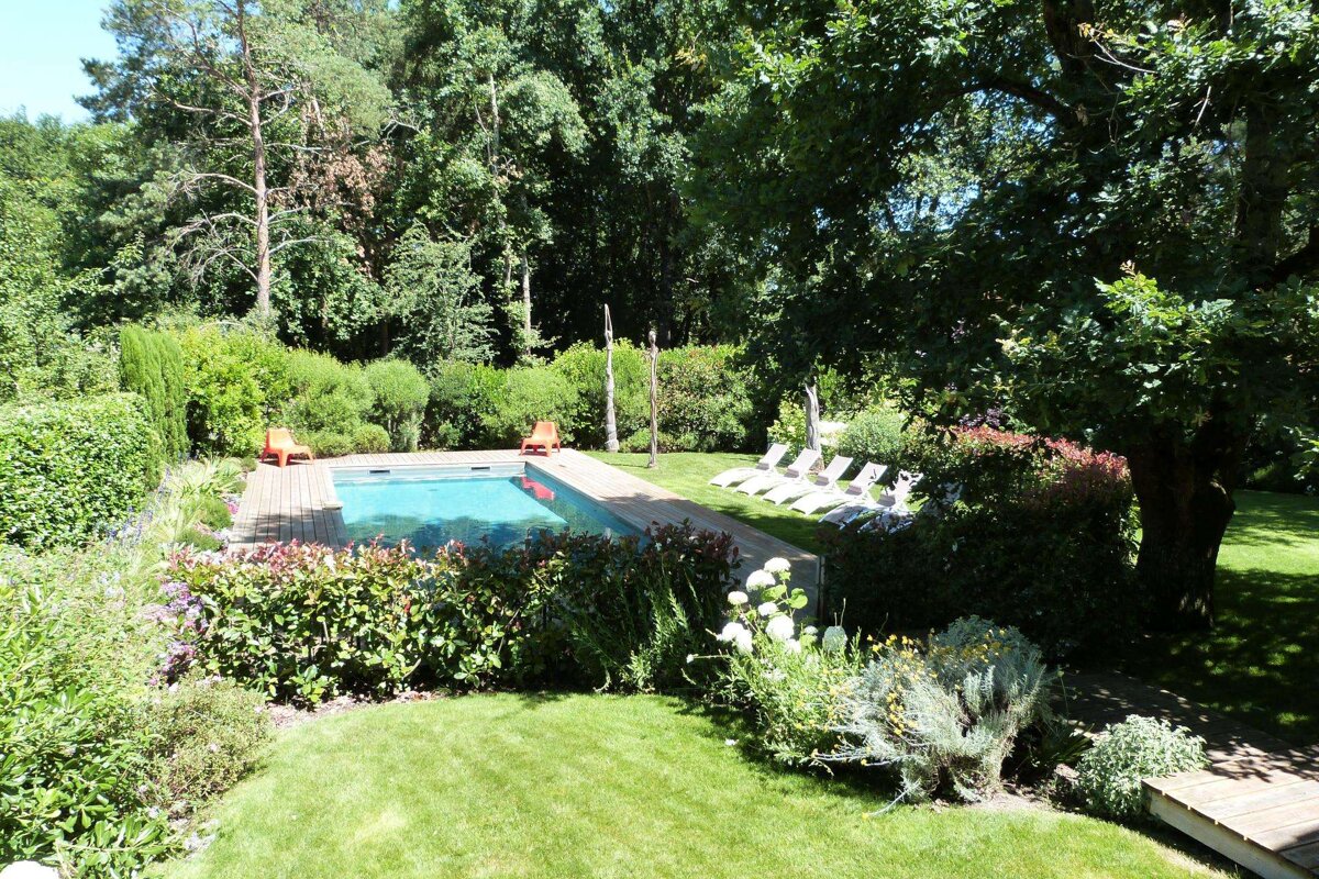A large swimming pool is surrounded by a lush green garden