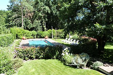 A large swimming pool is surrounded by a lush green garden