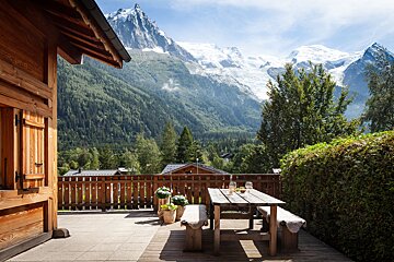 A patio with a table and benches with mountains in the background