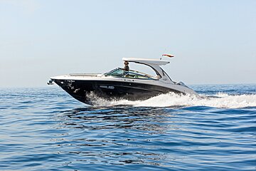 A sleek black and white motorboat cruising fast across calm blue water under a clear sky.