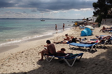 people sat on blue sun loungers on a small beach