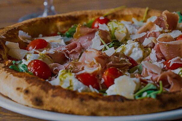 Appetizing pizza topped with prosciutto, cherry tomatoes, fresh mozzarella, arugula, and parmesan on a golden, bubbly crust.