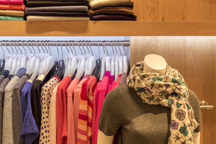 A mannequin wearing a scarf is in a closet full of clothes