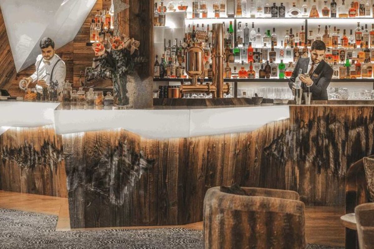 Two bartenders are preparing drinks at a bar with bottles of alcohol on shelves