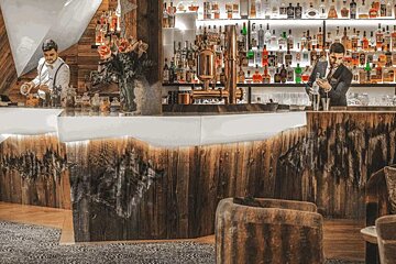 Two bartenders are preparing drinks at a bar with bottles of alcohol on shelves