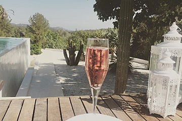 A glass of champagne sits on a wooden table next to a lantern