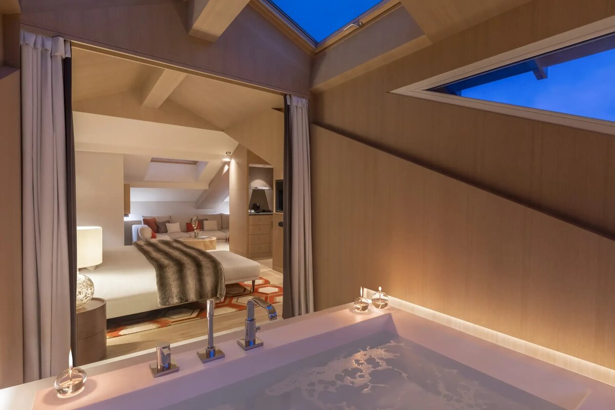 A bathtub in a hotel room with a bed in the background
