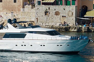 A large white yacht is floating in the water near a stone wall