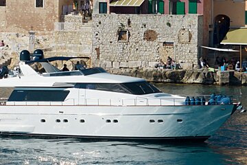 A large white yacht is floating in the water near a stone wall