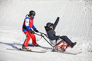 A person in a wheelchair is being pulled by a person on skis