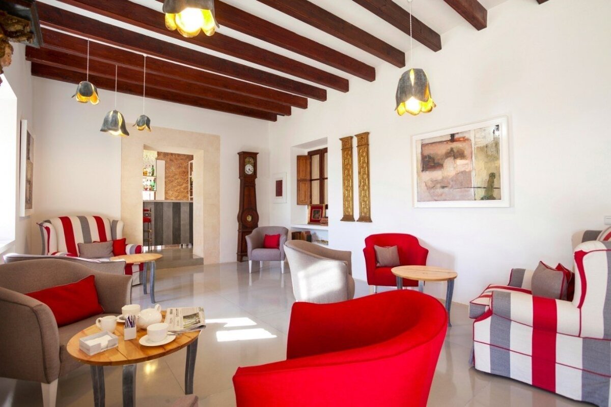 Bright, modern lounge with white walls, dark wood beams, and colorful seating (red, striped). Includes a grandfather clock and a bar area view.