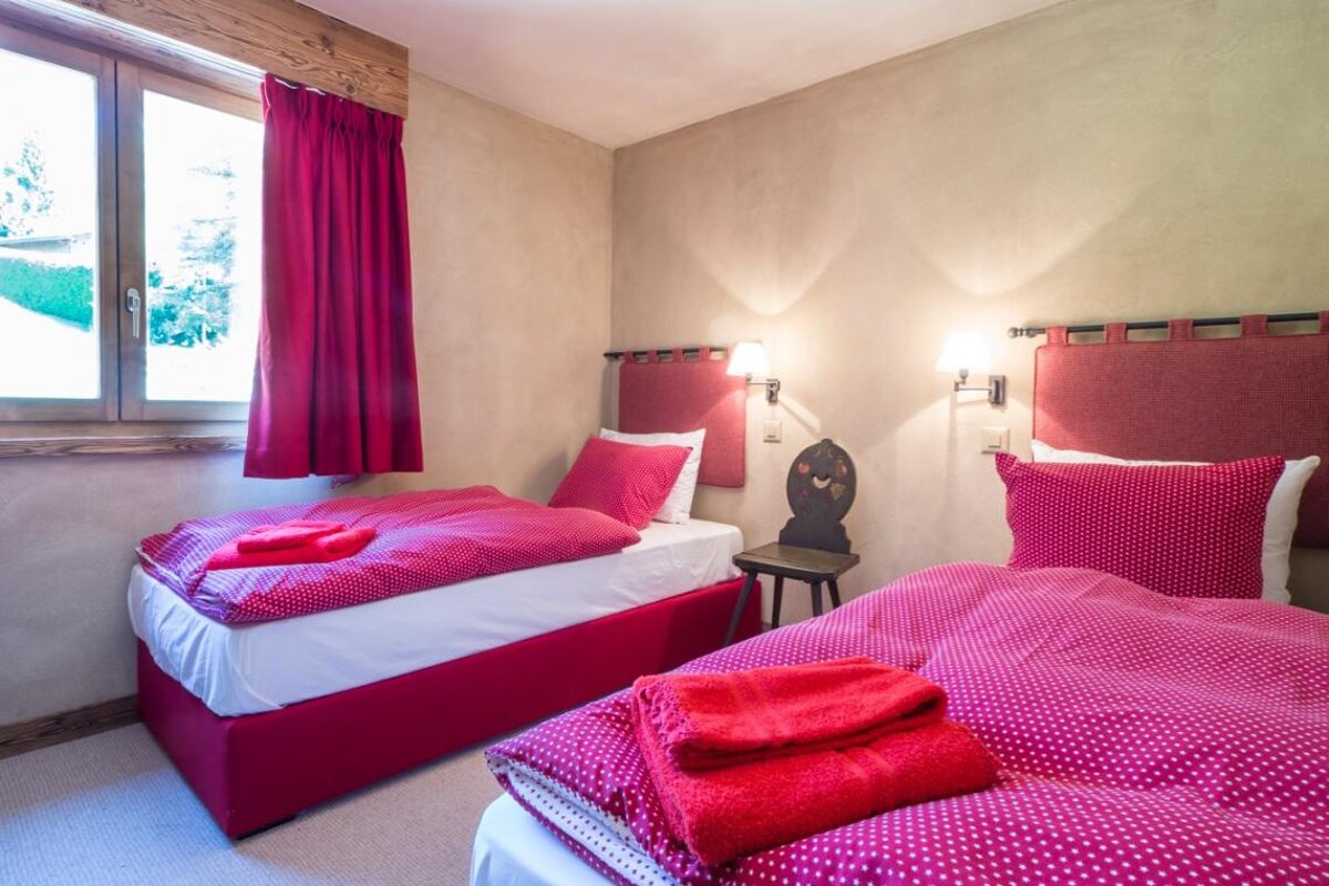 A bedroom with two beds and a window with red curtains