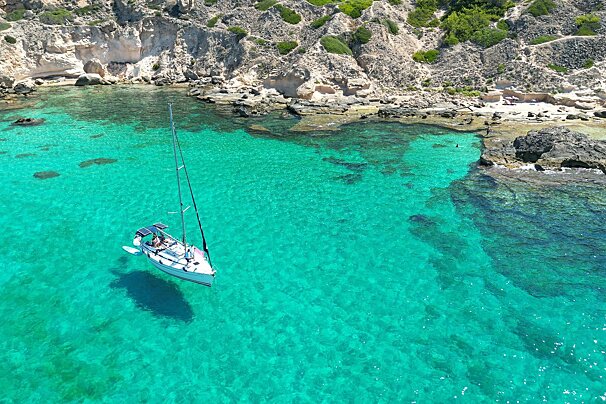A sailboat is floating in the water near a rocky shoreline