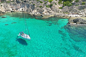 A sailboat is floating in the water near a rocky shoreline