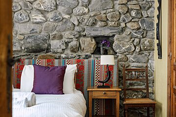 A bed with purple pillows in front of a stone wall