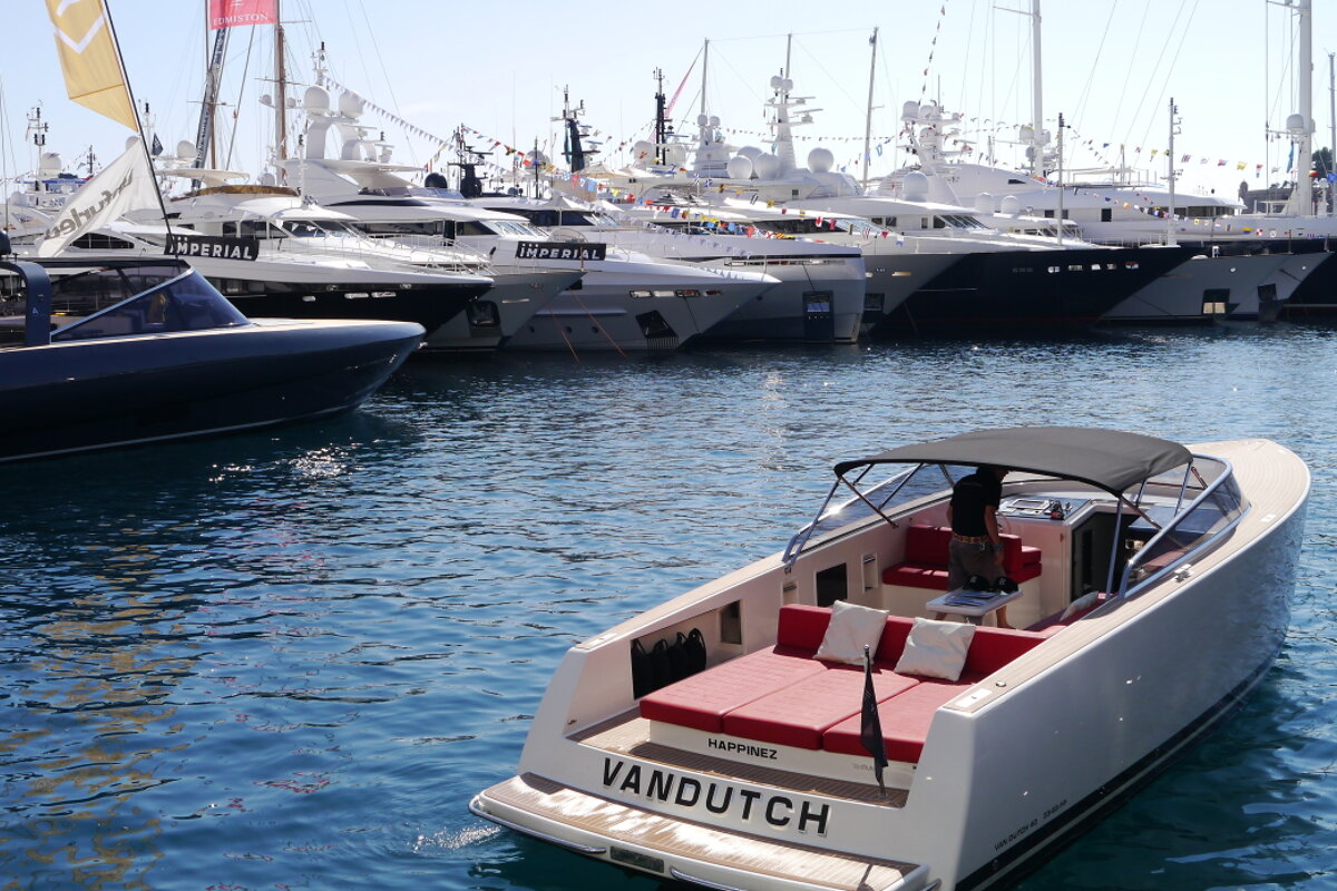 a small motor boat in water with superyachts in background, monaco