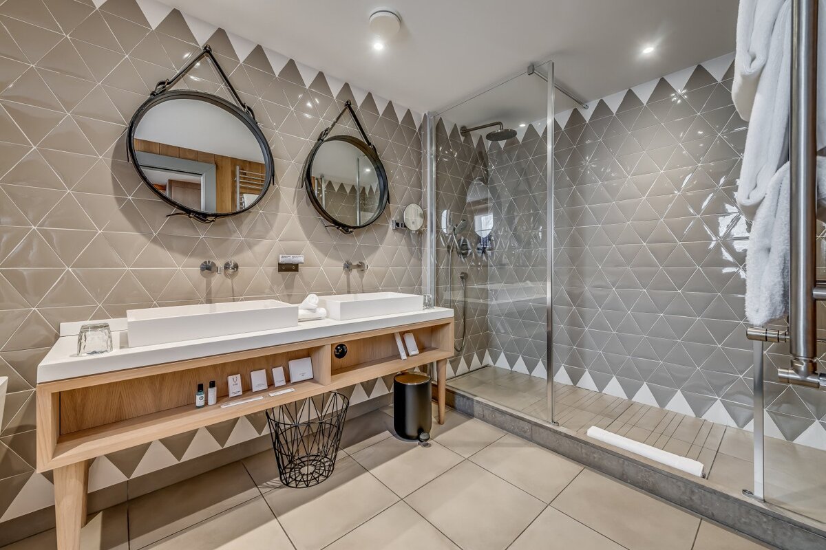 A contemporary bathroom featuring a double vanity with twin sinks, a glass-enclosed shower, and walls adorned with geometric triangular tiles.