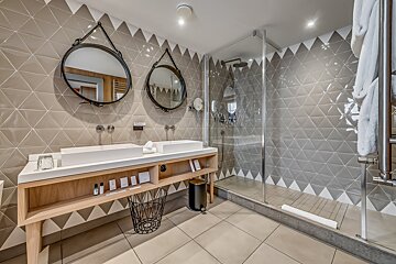 A contemporary bathroom featuring a double vanity with twin sinks, a glass-enclosed shower, and walls adorned with geometric triangular tiles.