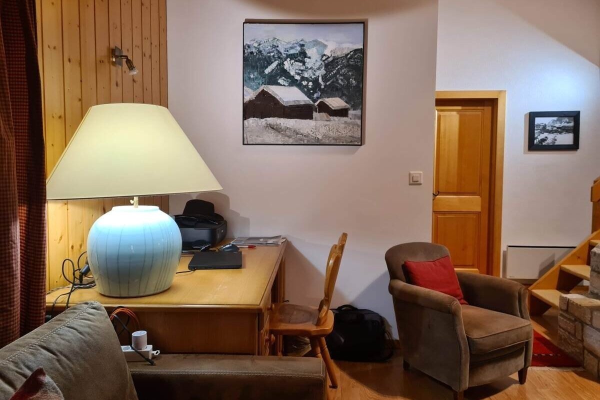 Cozy room with a large desk lamp, a mountain cabin painting, a brown armchair, and wood accents, creating a warm, inviting atmosphere.