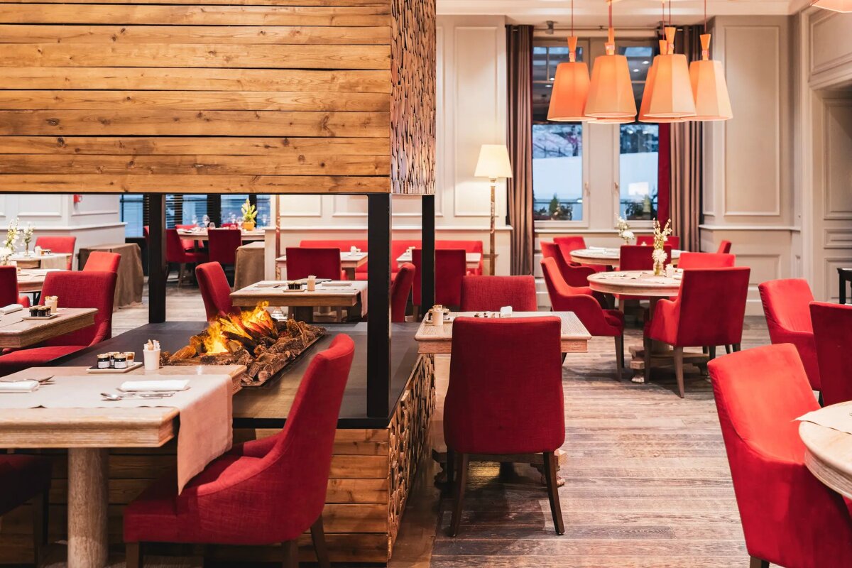 A restaurant with red chairs and tables and a fireplace