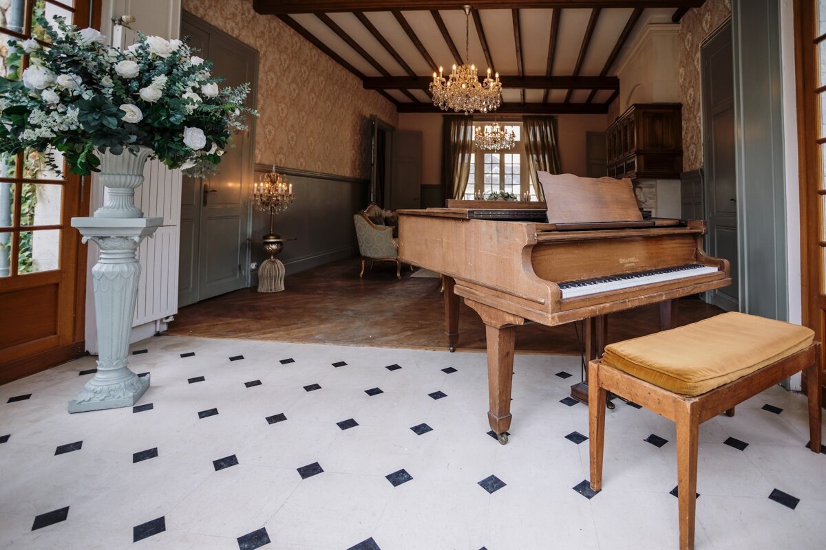 A piano sits in a room with a chandelier hanging from the ceiling