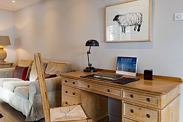 A cozy home office with a wooden desk and chair, a sofa in the background, and a unique sheep painting adorning the wall.