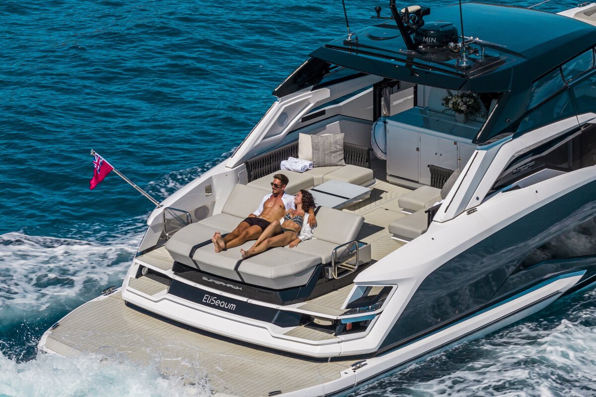 A couple relaxes, sunbathing on the aft deck of a luxurious yacht, cruising on sparkling blue ocean waters under the sun.
