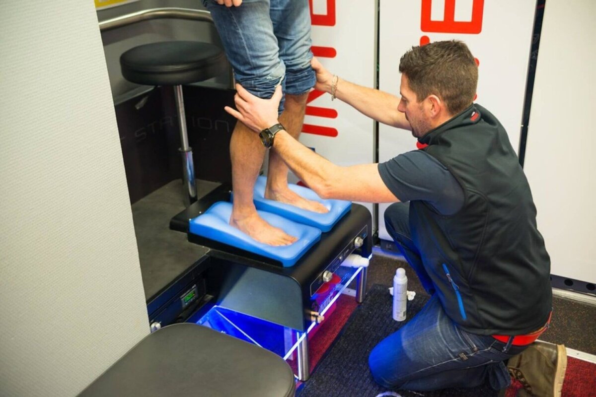 A man in a black vest is kneeling next to a person 's feet
