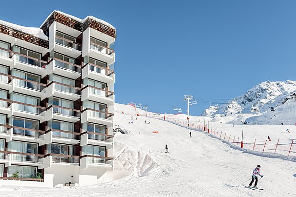 A person skiing down a snowy slope in front of a building