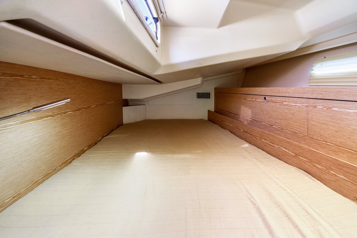 Interior of a boat's small sleeping cabin with wood-paneled walls, a low ceiling, and a beige mattress.