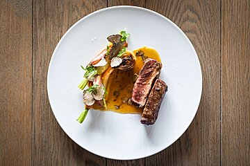 A white plate topped with meat and vegetables on a wooden table