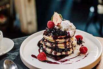 A stack of pancakes with blueberry sauce and raspberries on top