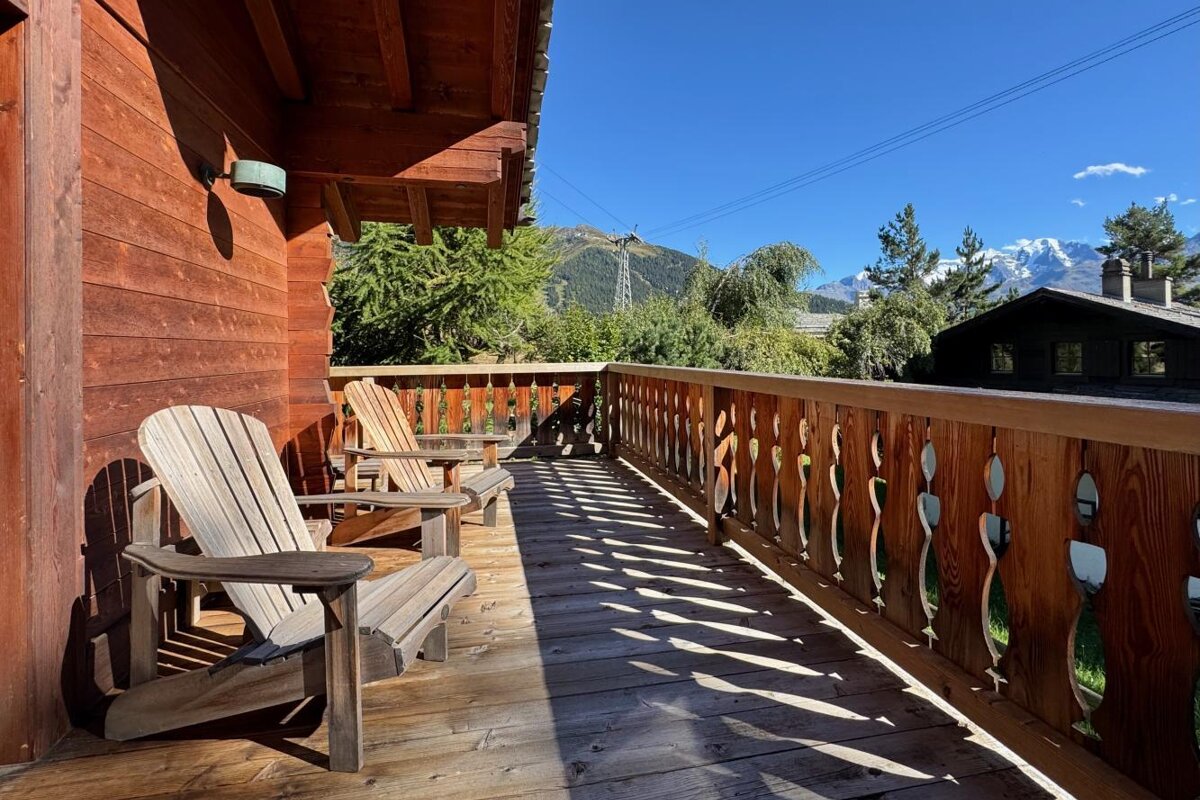 A wooden deck with chairs and mountains in the background