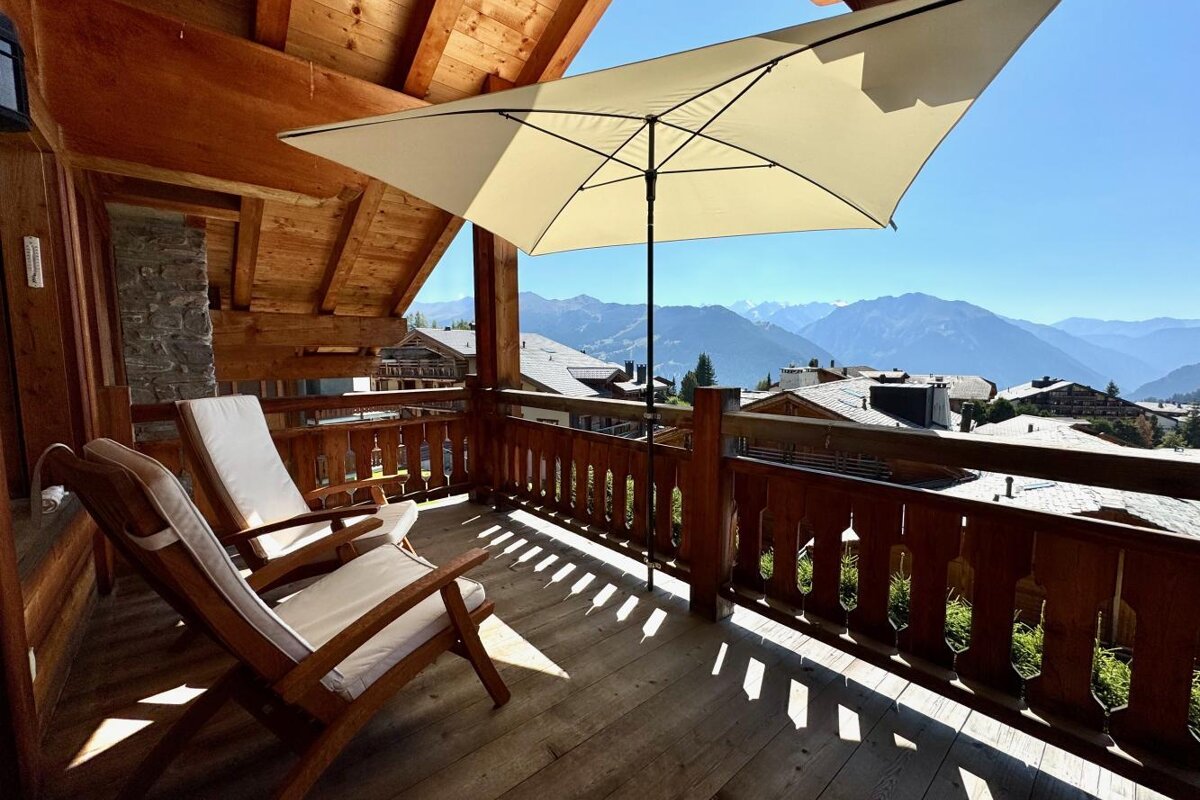 A balcony with two chairs and an umbrella with mountains in the background