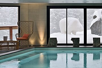 An indoor pool area with wicker furniture and a snowy mountain view outside, featuring a large snow-covered polar bear sculpture.